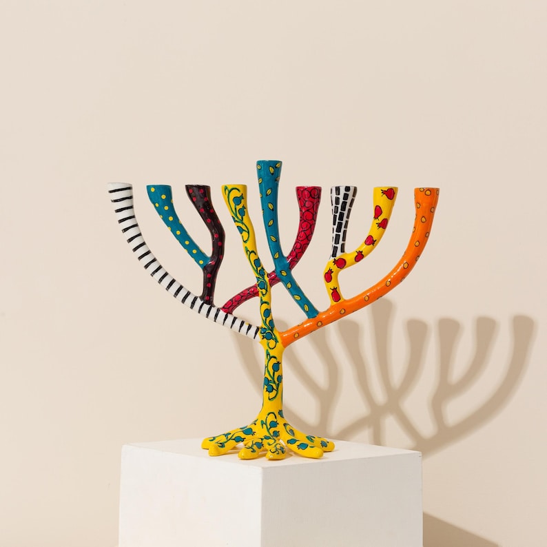 May include: A colorful menorah with a tree-like design. The branches are painted with different patterns, including stripes, polka dots, and floral designs. The base of the menorah is yellow and has a tree-like design.