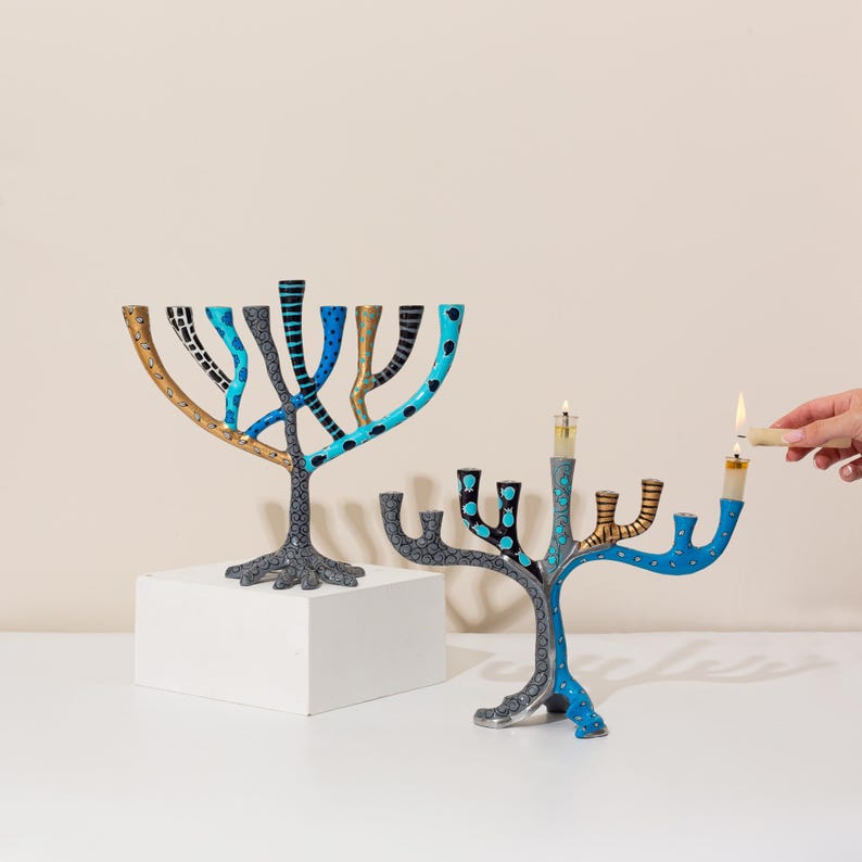 May include: Two blue and gold menorahs with a tree-like design. The menorahs are decorated with black and white polka dots, stripes, and animal print. One menorah has a lit candle.