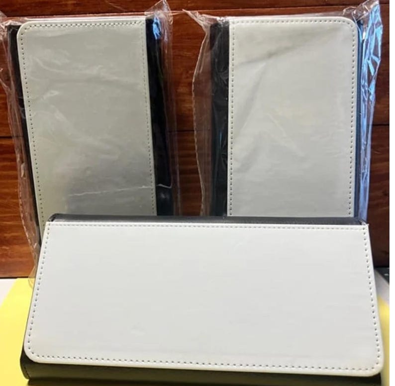 May include: Three white and black wallets, each in a protective plastic sleeve. The wallets have a white front with a black border and a stitched edge. The wallets are rectangular and appear to be made of a smooth material.