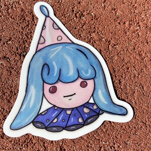 Puede incluir: Un personaje de dibujos animados azul y rosa con un gorro de fiesta, que lleva un vestido azul y blanco con lunares blancos. El personaje tiene una cara rosa con ojos rojos y una pequeña sonrisa.