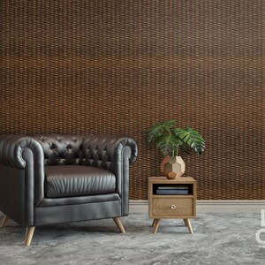 Puede incluir: Un sill&oacute;n de cuero negro con tapicer&iacute;a capiton&eacute; y patas de madera se encuentra frente a una pared con un patr&oacute;n tejido marr&oacute;n. Una peque&ntilde;a mesa auxiliar de madera con un caj&oacute;n y una planta en maceta se encuentra junto al sill&oacute;n.