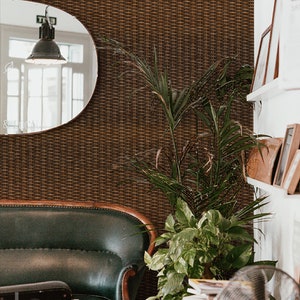 Puede incluir: Un sof&aacute; de cuero verde con patas de madera se encuentra en una habitaci&oacute;n con un revestimiento de pared tejido marr&oacute;n. Una gran planta en maceta con hojas verdes se encuentra en la esquina de la habitaci&oacute;n. Un ventilador plateado se encuentra en el suelo junto a una pila de libros.