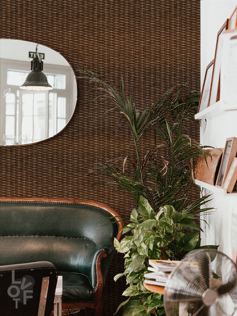 Puede incluir: Un sof&aacute; de cuero verde con patas de madera se encuentra en una habitaci&oacute;n con un revestimiento de pared tejido marr&oacute;n. Una gran planta en maceta con hojas verdes se encuentra en la esquina de la habitaci&oacute;n. Un ventilador plateado se encuentra en el suelo junto a una pila de libros.