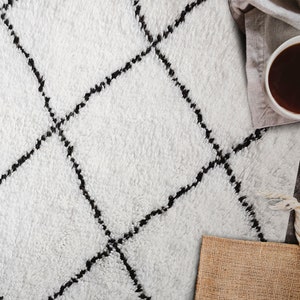 May include: A white fluffy rug with a black diamond pattern. The rug is on a wooden floor with a cup of coffee and a burlap sack in the background.