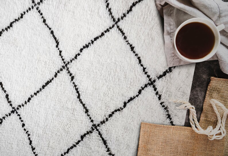 May include: A white fluffy rug with a black diamond pattern. The rug is on a wooden floor with a cup of coffee and a burlap sack in the background.