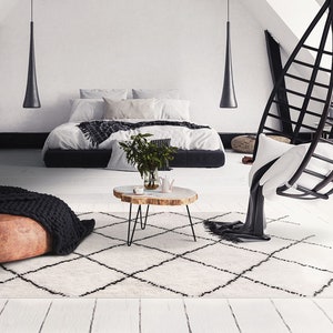 May include: A white and black patterned rug with a brown leather ottoman, a black knitted throw blanket, a wooden coffee table, and a black hanging chair with a white cushion in a modern living room.