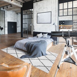 May include: A modern loft bedroom with a gray bed, a white and black patterned rug, two brown leather chairs, and a telescope on a tripod.