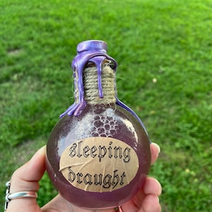 May include: A small glass bottle with a purple wax seal and a brown label that reads "sleeping draught". The bottle is filled with a purple liquid and has a white string tied around the neck.