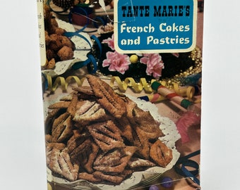 May include: A vintage cookbook titled "Tante Marie's French Cakes and Pastries" with a blue and white label. The cover features images of pastries, cakes, and decorative elements. The book has a worn appearance, suggesting age and use.