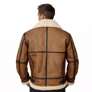 May include: Brown leather jacket with a cream-colored shearling collar and lining. The jacket features black trim and a classic design. A warm and stylish outerwear piece.