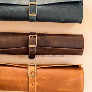 May include: Three leather rolls with brass buckles. The rolls are in different colors: dark blue, brown, and tan.