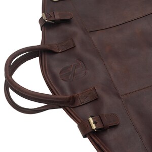 May include: A brown leather guitar case with a double handle and multiple buckles. The case has a logo embossed on the front.