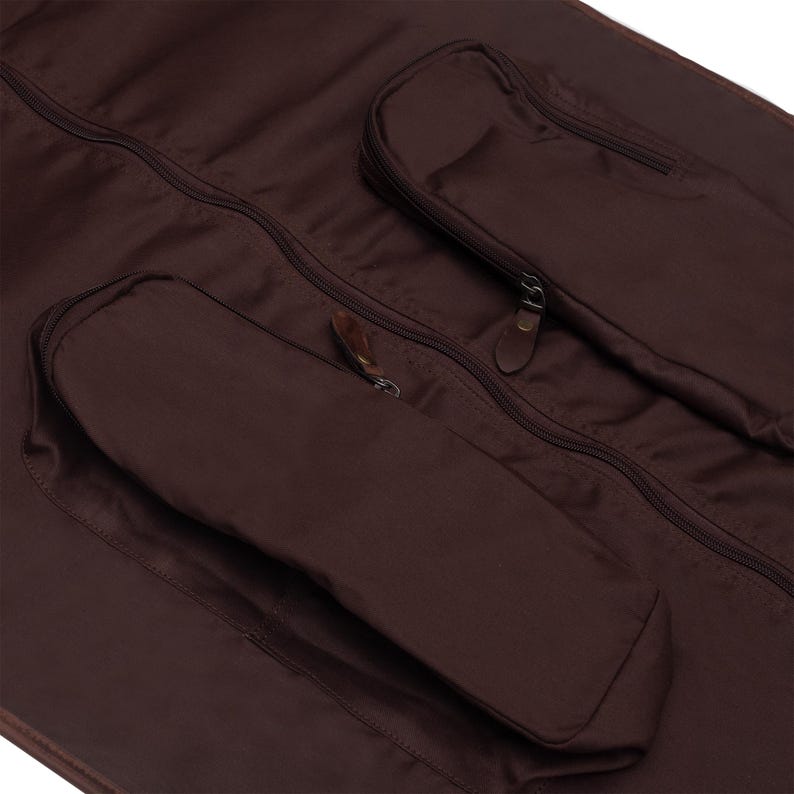 May include: A brown garment bag with two zippered pockets and a brown leather zipper pull.