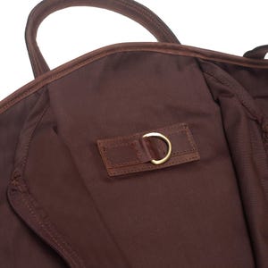 May include: A brown leather garment bag with a zipper closure and a leather strap with a metal ring.