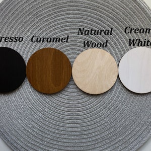 Puede incluir: Cuatro posavasos redondos de madera en diferentes colores: negro, marr&oacute;n, marr&oacute;n claro y blanco. Los posavasos est&aacute;n etiquetados como "Espresso", "Caramelo", "Madera natural" y "Blanco cremoso".