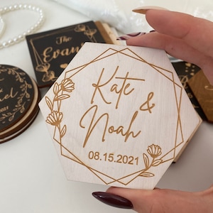 Puede incluir: Un letrero hexagonal de madera con un marco geom&eacute;trico dorado y detalles florales. El letrero dice "Kate & Noah" con la fecha "08.15.2021" debajo.