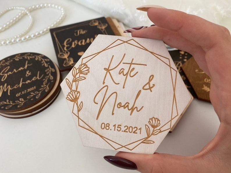 Puede incluir: Un letrero hexagonal de madera con un marco geom&eacute;trico dorado y detalles florales. El letrero dice "Kate & Noah" con la fecha "08.15.2021" debajo.