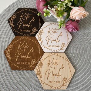 Puede incluir: Cuatro posavasos hexagonales de madera con un dise&ntilde;o geom&eacute;trico dorado y detalles florales. Cada posavasos tiene el texto "Kate & Noah" y la fecha "08.15.2021".
