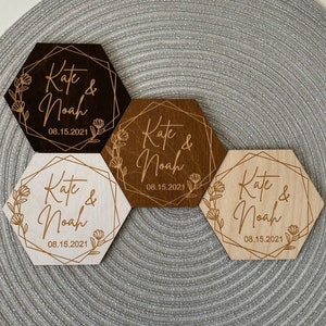 Puede incluir: Cuatro posavasos hexagonales de madera con un dise&ntilde;o geom&eacute;trico y detalles florales. Los posavasos est&aacute;n grabados con los nombres "Kate & Noah" y la fecha "08.15.2021". Los posavasos son de diferentes tonos de marr&oacute;n y madera natural.