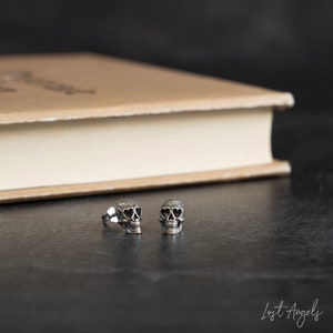 May include: A pair of silver skull earrings with heart-shaped sunglasses. The earrings are small and delicate, and they would make a great gift for a friend or loved one.