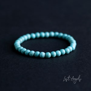 Puede incluir: Un brazalete de cuentas de color azul turquesa con un diseño sencillo. El brazalete está hecho de pequeñas cuentas redondas que están enhebradas en un cordón delgado.