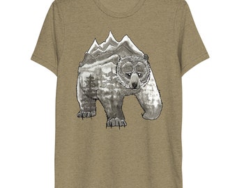 Può includere: T-shirt beige a maniche corte con un'illustrazione in bianco e nero di un orso. L'orso ha una catena montuosa sulla schiena. L'orso cammina in avanti, con montagne e alberi dettagliati.