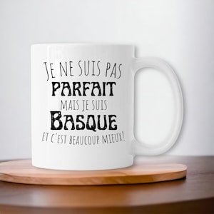 Może przedstawiać: Biały kubek ceramiczny z czarnym tekstem, który brzmi "Je ne suis pas parfait mais je suis Basque et c'est beaucoup mieux!"