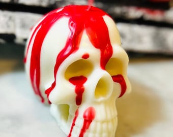 May include: A white skull-shaped candle with red wax dripping down the sides. The candle has a realistic skull design, perfect for Halloween or gothic decor. The red wax creates a striking contrast against the white candle.