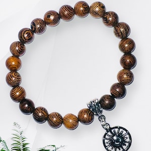 May include: A brown wooden beaded bracelet with a silver charm featuring a sun design.