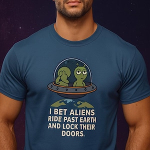 May include: Teal blue t-shirt featuring a cartoon image of two aliens in a spaceship above Earth. The text reads, "I BET ALIENS RIDE PAST EARTH AND LOCK THEIR DOORS." The shirt is made of a soft material.
