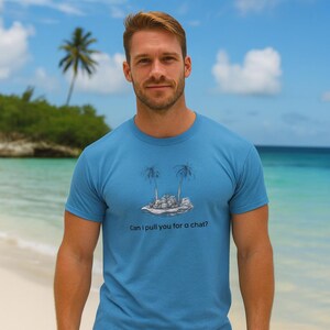 May include: A light blue t-shirt featuring a tropical island graphic with two palm trees and the text "Can I pull you for a chat?". The shirt is made of a soft material and is suitable for casual wear.