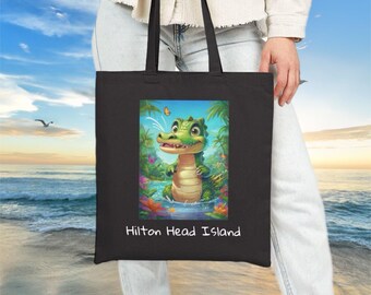 May include: Black tote bag featuring a colorful illustration of a cartoon alligator in a tropical setting. The alligator is green and yellow, standing in water with flowers and palm trees. The text "Hilton Head Island" is printed below the image.