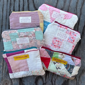 Könnte beinhalten: Eine Sammlung handgefertigter Patchwork-Reißverschlusstaschen in verschiedenen Farben und Mustern. Jede Tasche weist eine einzigartige Kombination aus Stoffen auf, darunter Blumenmuster und unifarbene Stoffe. Der Text "PINK POSSUM STUDIO" ist sichtbar.