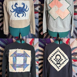 Puede incluir: Cuatro sudaderas con diseños acolchados únicos. Una sudadera beige presenta un cangrejo azul. Una sudadera gris tiene un patrón geométrico en rosa y verde. Una sudadera negra muestra un bloque de edredón cuadrado. Otra sudadera negra tiene un diseño de cesta.