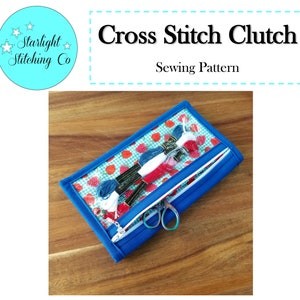 May include: A blue cross stitch clutch with a zipper closure and a clear plastic window. The window shows a strawberry patterned fabric with white embroidery floss inside. The clutch is on a wooden surface. Cross Stitch Clutch Sewing Pattern.