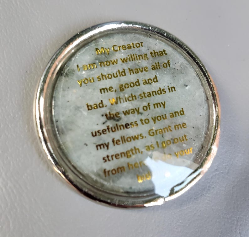 May include: A circular silver-toned token featuring a light gray, speckled stone-like center. Gold text is printed on the surface, reading: My Creator I am now willing that you should have all of me, good and bad. Which stands in the way of my usefulness to you and my fellows. Grant me strength, as I go out from here to do your bidding.