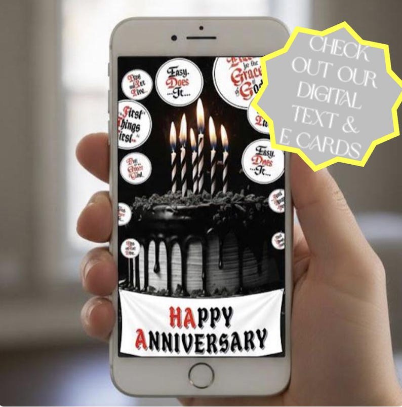May include: A smartphone screen displays a digital graphic of a dark chocolate cake with lit candles, surrounded by circular text bubbles featuring phrases like Easy Does It and First Things First, with a banner reading Happy Anniversary at the bottom.
