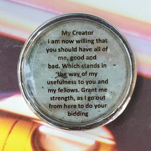 May include: A circular silver-toned metal charm featuring a light gray speckled background under a clear glass dome. The text reads: My Creator I am now willing that you should have all of me, good and bad. Which stands in the way of my usefulness to you and my fellows. Grant me strength, as I go out from here to do your bidding.