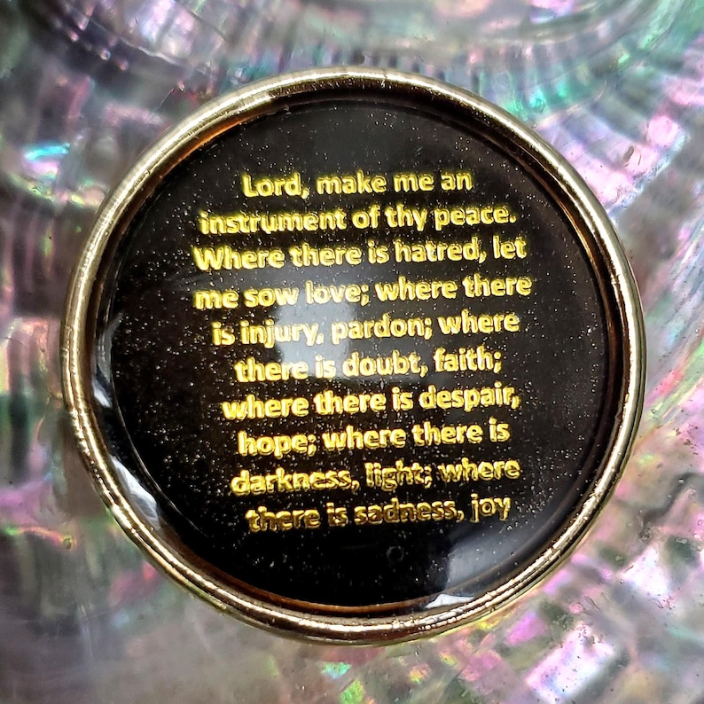 Peut inclure: Un objet d&eacute;coratif rond noir et or avec du texte dor&eacute;. Le texte dit : &laquo; Seigneur, fais de moi un instrument de ta paix &raquo;. L'objet a un fond iris&eacute; et r&eacute;fl&eacute;chissant.