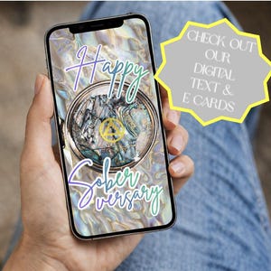 Peut inclure: Un smartphone affiche une carte &eacute;lectronique num&eacute;rique avec les mots "Happy Soberversary" en &eacute;criture cursive. La carte pr&eacute;sente un motif circulaire avec un embl&egrave;me dor&eacute; et le texte "Years of Recovery". Une forme d'&eacute;clat jaune contient le texte "Check out our digital text & e-cards."