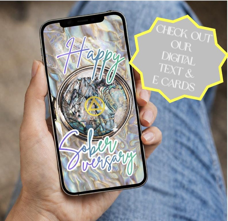 Peut inclure: Un smartphone affiche une carte &eacute;lectronique num&eacute;rique avec les mots "Happy Soberversary" en &eacute;criture cursive. La carte pr&eacute;sente un motif circulaire avec un embl&egrave;me dor&eacute; et le texte "Years of Recovery". Une forme d'&eacute;clat jaune contient le texte "Check out our digital text & e-cards."