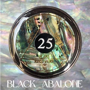 May include: A circular medallion featuring an iridescent abalone shell inlay. A black center circle displays the number 25 in white. A gold triangle surrounds the center, with the words UNITY, SERVICE, and YEARS RECOVERY, and Roman numerals.