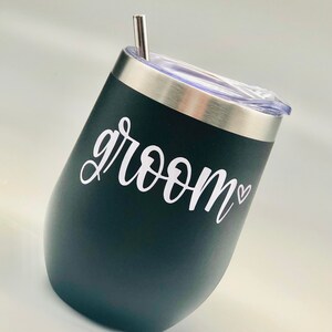 K&ouml;nnte beinhalten: Schwarzer Edelstahlbecher mit durchsichtigem Deckel und Strohhalm. Auf dem Becher steht in wei&szlig;er Schrift "groom" in Kursivschrift mit einem kleinen Herz.