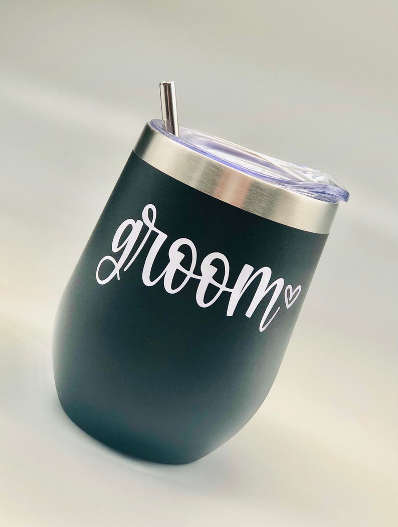 K&ouml;nnte beinhalten: Schwarzer Edelstahlbecher mit durchsichtigem Deckel und Strohhalm. Auf dem Becher steht in wei&szlig;er Schrift "groom" in Kursivschrift mit einem kleinen Herz.