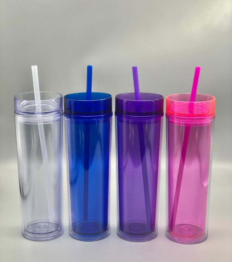 K&ouml;nnte beinhalten: Vier transparente Doppelwandbecher mit farbigen Deckeln und Strohhalmen. Die Becher sind mit einer klaren Fl&uuml;ssigkeit gef&uuml;llt. Die Deckel und Strohhalme sind blau, lila und rosa. Der erste Becher ist transparent mit einem wei&szlig;en Strohhalm.
