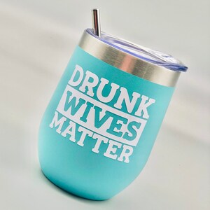 May include: A light blue stainless steel tumbler with a white lid and a straw. The tumbler has the text "DRUNK WIVES MATTER" printed on it.