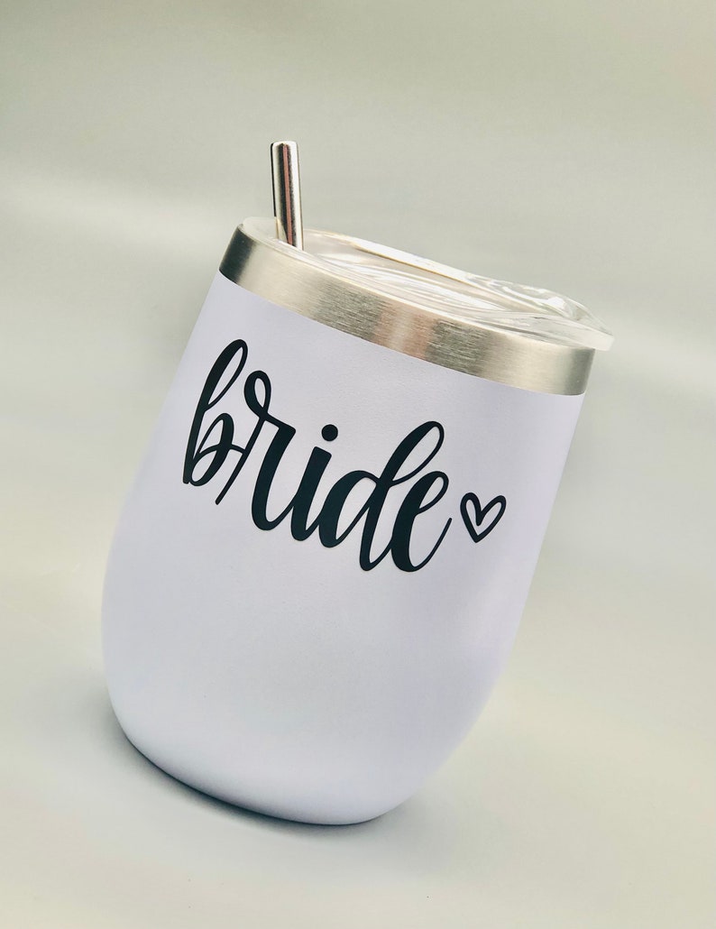 K&ouml;nnte beinhalten: Ein wei&szlig;er Edelstahlbecher mit einem schwarzen Vinyl-Aufkleber, auf dem "bride" mit einem kleinen Herzen steht. Der Becher hat einen Deckel und einen Strohhalm.