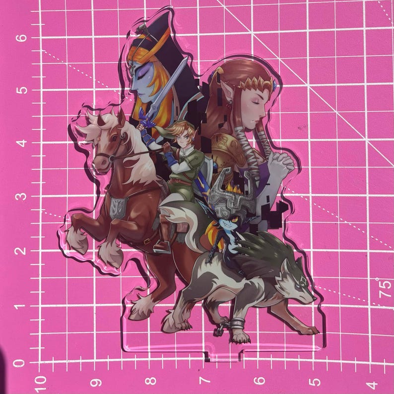 May include: A clear acrylic standee featuring characters from The Legend of Zelda series. The design includes Link on horseback, a wolf, and other characters in a colorful, detailed illustration. The standee is on a pink grid background.
