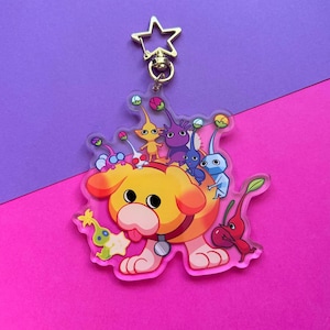 May include: A yellow dog character with a red collar and a group of colorful creatures on its back. The dog is standing on a clear acrylic keychain.
