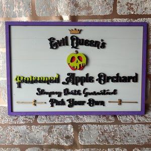 May include: Wooden sign with a purple frame and white background. The sign reads "Evil Queen's Poisoned Apple Orchard" with a gold crown and a green and red apple. The text "Sleeping Death Guaranteed, Pick Your Own" is also included.